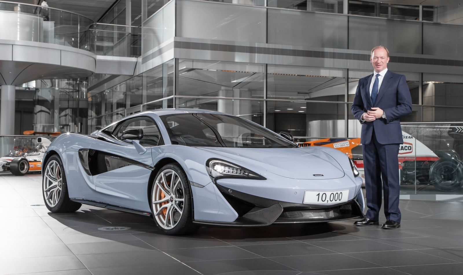 Een man in pak staat naast een blauwe McLaren.