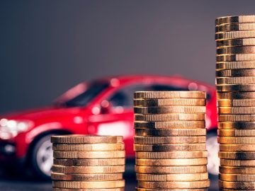 Een stapel munten voor een rode auto, symbool voor de afbouw BPM voor goedkopere auto's.