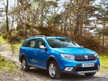Een blauwe Dacia Logan MCV Stepway geparkeerd op een onverharde weg in het bos.