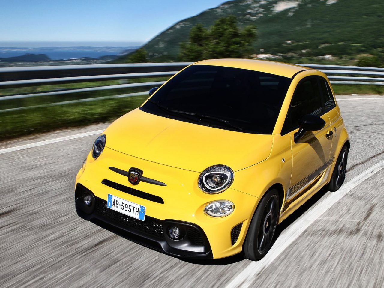 Een gele Fiat 500 die over een bergweg rijdt, weergegeven als Daily #76 op AutoRAI.