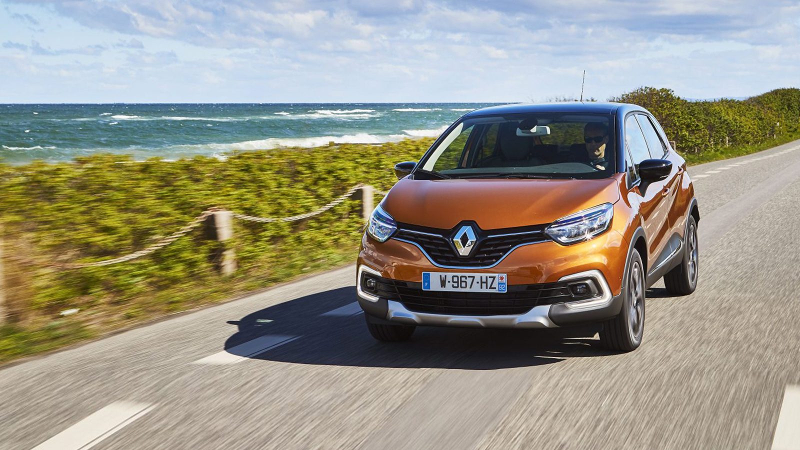 De Vernieuwde Renault Captur rijdt over een weg vlakbij de oceaan.