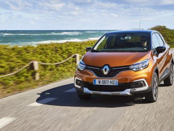 De Vernieuwde Renault Captur rijdt over een weg vlakbij de oceaan.