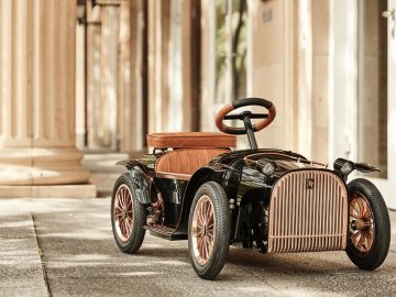 Een kleine zwart-bruine elektrische loopauto geparkeerd op een trottoir.