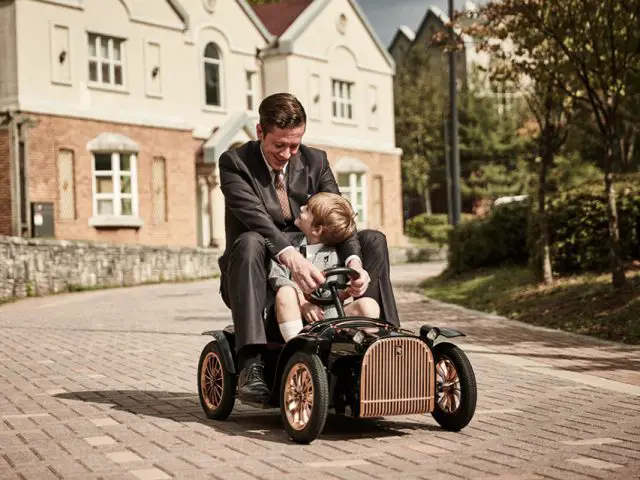 Een man in pak rijdt met zijn zoon in een elektrische loopauto van 3.000 dollar.