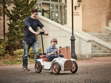 Een man en een jongen rijden op een elektrische loopauto van 3.000 dollar.