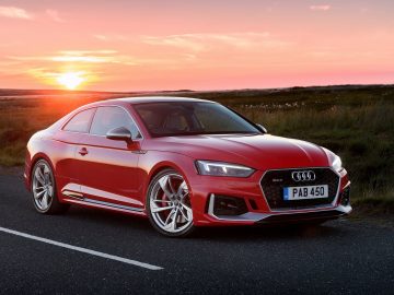 De rode Audi RS 5 coupé rijdt bij zonsondergang over de weg.