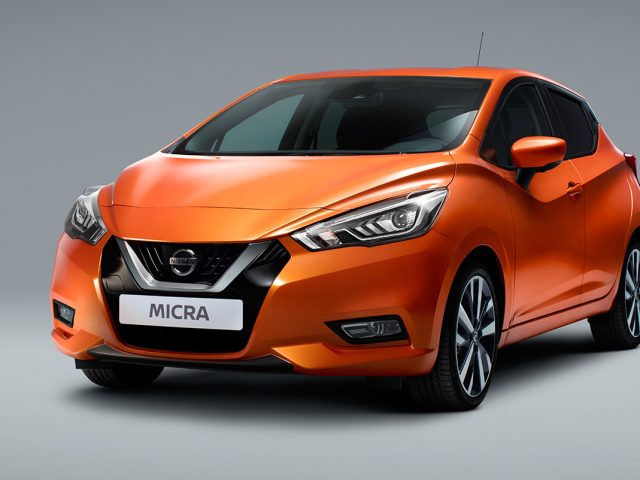 Een oranje Nissan Micra op een grijze achtergrond.