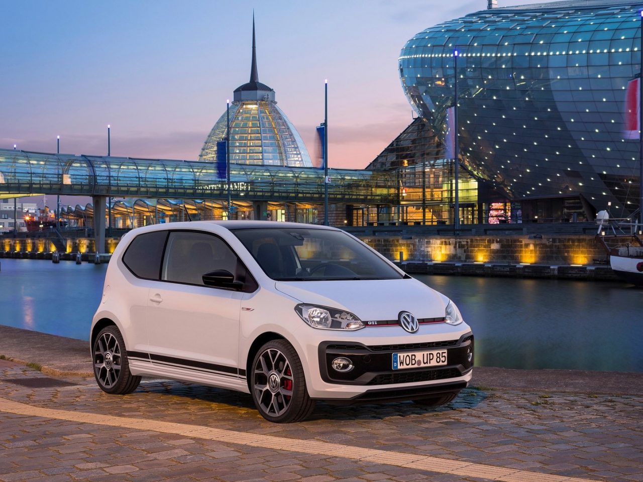 Een witte Volkswagen Up geparkeerd voor een gebouw 's nachts.