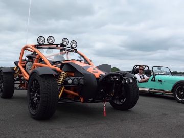Een groen-oranje Ariel Nomad staat geparkeerd naast een man.