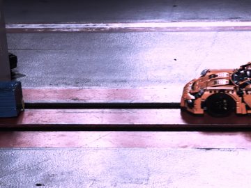 Een oranje Lego-auto staat op een baan in een garage.