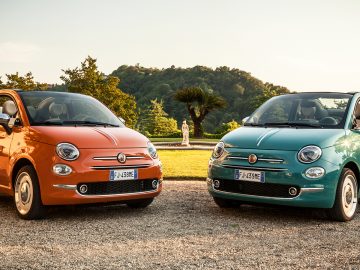 Twee oranje en blauwe Fiat 500 Anniversario-auto's geparkeerd voor een huis.