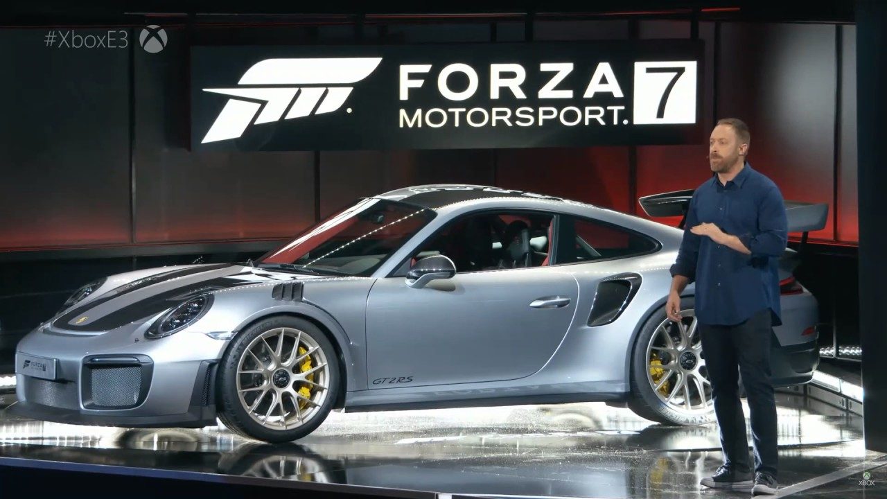 Een man staat naast een Porsche 911 GT2 RS op een podium op de gamebeurs E3.