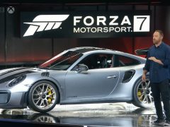 Een man staat naast een Porsche 911 GT2 RS op een podium op de gamebeurs E3.