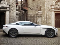 De witte Aston Martin DB11 staat geparkeerd voor een oud gebouw.