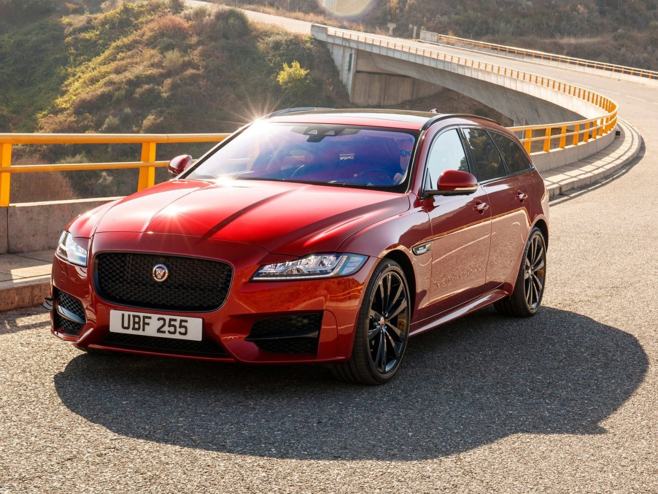 De rode Jaguar XF Sportbrake rijdt op een brug.