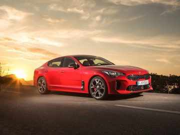 De rode Kia Stinger, voorzien van koolstofremschijven, rijdt bij zonsondergang over de weg.