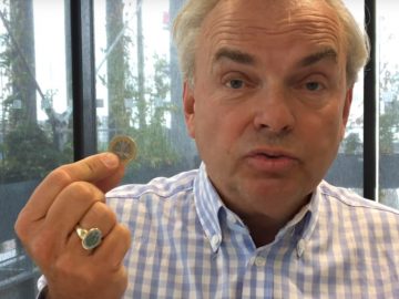 Een man houdt een munt in zijn hand voor een videokolom.