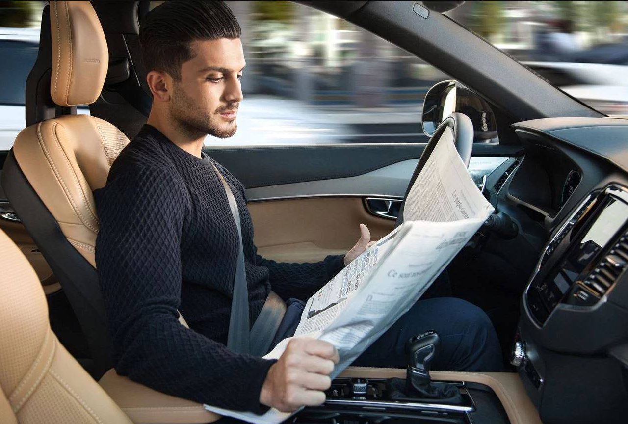 Een man in een auto die een krant leest tijdens autonoom rijden.