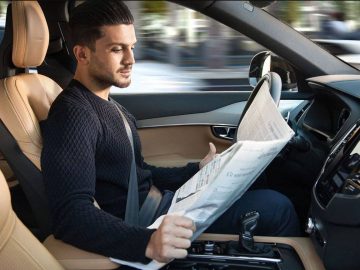 Een man in een auto die een krant leest tijdens autonoom rijden.