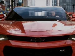 Een rode Chevrolet Camaro uit 2018 verschijnt in The Crew 2 en rijdt door een stadsstraat.