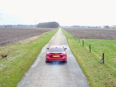 Een rode auto die in 2017 over een onverharde weg in een veld rijdt.
