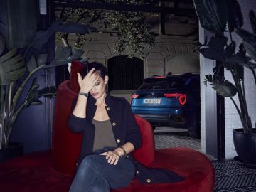Een vrouw zit op een rode stoel voor een auto van Lynk & Co en neemt haar bestellingen door.