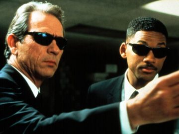 Twee mannen in het zwart in pak die een pistool op elkaar richten.