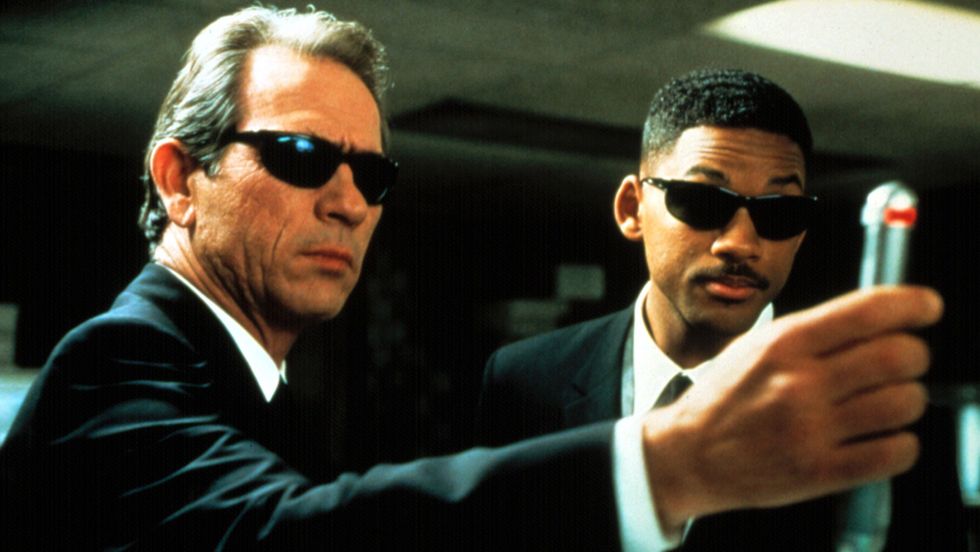 Twee mannen in het zwart in pak die een pistool op elkaar richten.