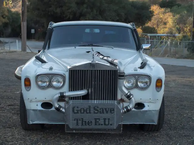 Een witte Rolls-Royce geparkeerd op een onverharde weg.