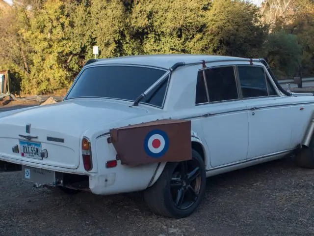 Een witte vintage auto, officieel de lelijkste Rolls-Royce, geparkeerd in een onverharde parkeerplaats.