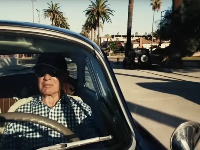 Een man rijdt in een Porsche 356 op een parkeerplaats.