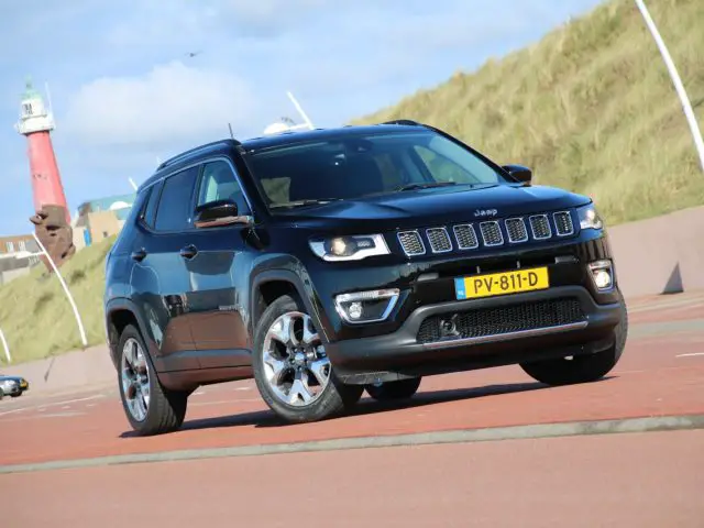 Een zwarte Jeep Compass rijdt over een weg.