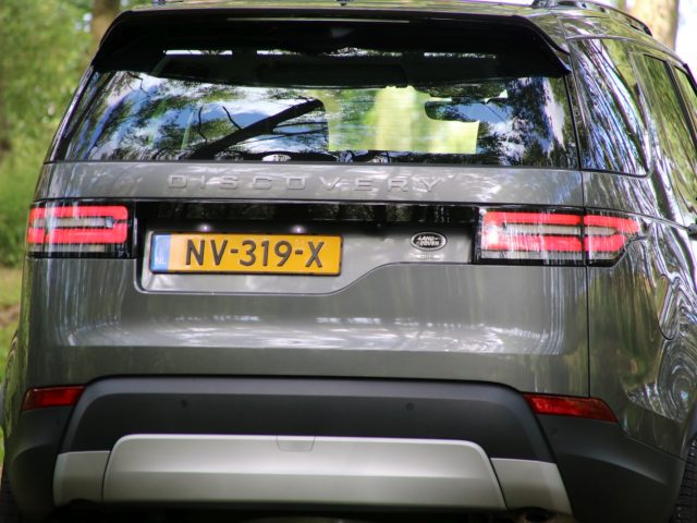 Een zilveren Land Rover Discovery staat geparkeerd in een bosrijke omgeving.
