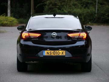 De achterkant van een zwarte Opel Insignia Grand Sport 1.5 Turbo geparkeerd op een parkeerplaats.