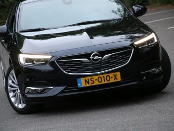 Een zwarte Opel Insignia Grand Sport 1.5 Turbo die over de weg rijdt.