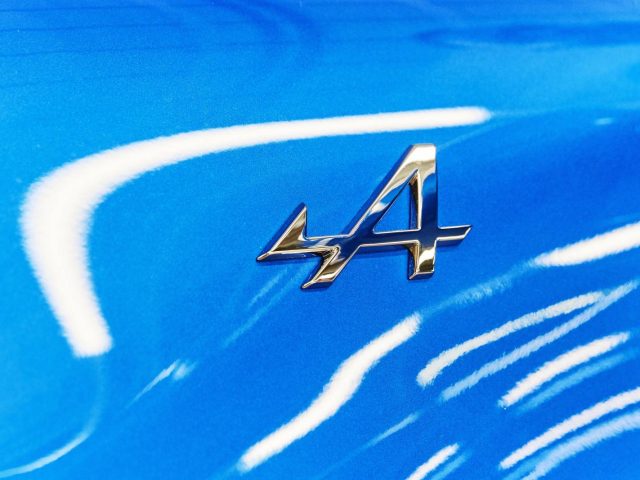 Een blauwe Alpine A110 met een zilveren embleem op de motorkap.