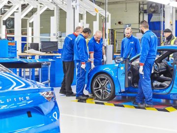 Een groep mannen werkt in een fabriek aan een A110 Alpine Blue-sportwagen.