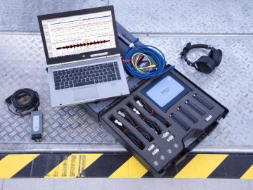 Een laptop staat naast een paar koptelefoons op een tafel, beide uitgevoerd aan kwaliteitscontrole bij Audi.