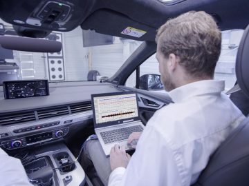 Een man die een laptop gebruikt op de achterbank van een Audi.