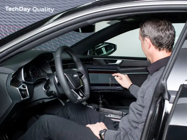 Een man zit op de bestuurdersstoel van een kwaliteitscontrole Audi.
