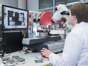 Een man in een laboratoriumjas die een kwaliteitscontrole uitvoert terwijl hij naar een microscoop kijkt.