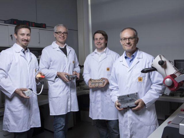 Vier mannen in laboratoriumjassen staan voor een microscoop voor Audi kwaliteitscontrole.