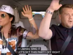 Twee mannen in een auto zwaaien met hun handen in de lucht tijdens Carpool Karaoke.