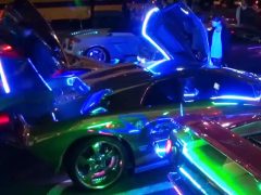 Een groep auto's, waaronder Lamborghini-rijders, parkeerde 's nachts op een neonverlichte parkeerplaats.