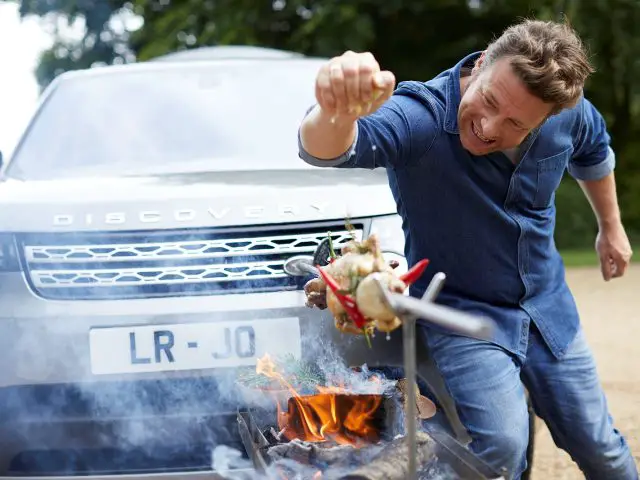 Een man grilt vlees op een barbecue voor een Land Rover Discovery.