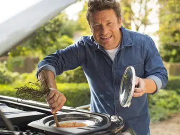 Een man bereidt barbecuevoedsel in de motorkap van een Land Rover Discovery.