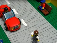Een legostraatbeeld met een schokkende rode auto en mensen.