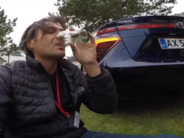 Een man dronk uit een fles naast een Toyota Avalon.