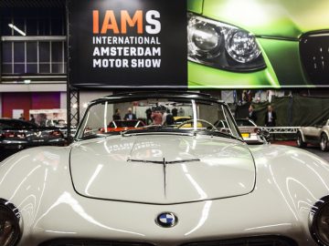 Een klassieke auto staat geparkeerd voor een bord met de tekst International Amsterdam Motor Show 2018.