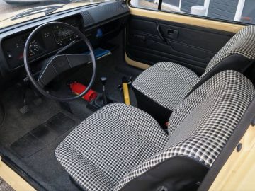 Het interieur van een gele Golf 38 jaar oud-auto met een geruit dashboard.